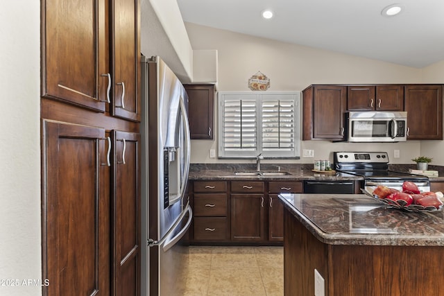 kitchen with appliances with stainless steel finishes, a sink, vaulted ceiling, light tile patterned floors, and dark stone countertops