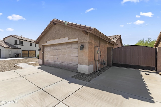 view of side of property featuring a gate, stucco siding, and an attached garage
