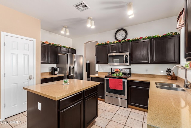 kitchen featuring light tile patterned floors, stainless steel appliances, light stone countertops, a kitchen island, and sink