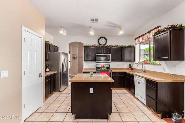 kitchen with light tile patterned floors, appliances with stainless steel finishes, a kitchen island, dark brown cabinetry, and sink