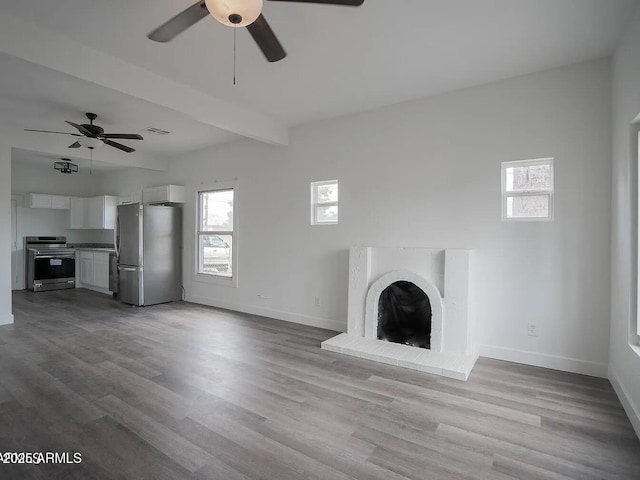 unfurnished living room featuring baseboards, visible vents, beamed ceiling, wood finished floors, and a brick fireplace