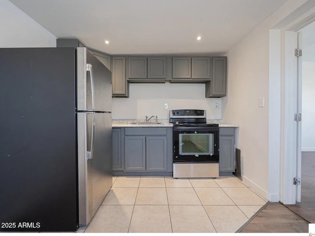 kitchen with gray cabinets, light countertops, electric range oven, freestanding refrigerator, and a sink