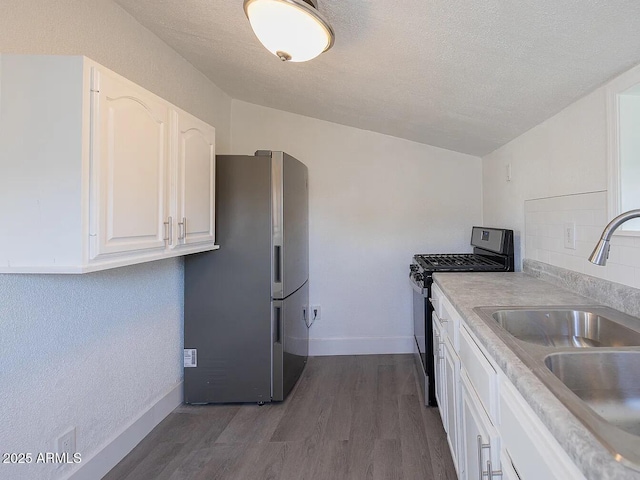 kitchen featuring lofted ceiling, stainless steel appliances, dark wood-style flooring, a sink, and white cabinets