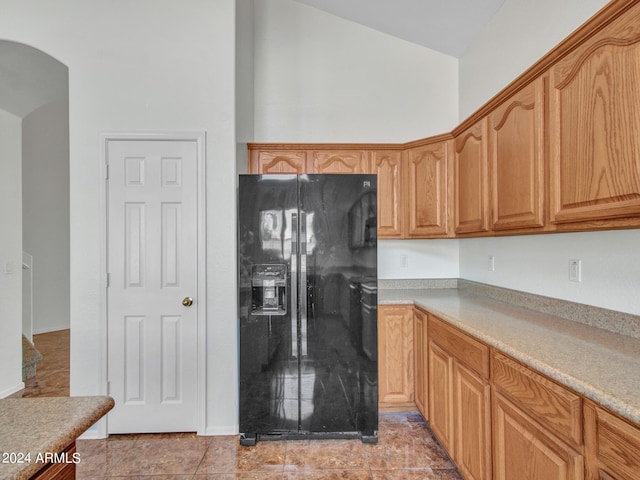 kitchen with light tile patterned floors, vaulted ceiling, and black fridge