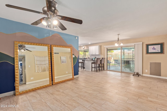 unfurnished living room featuring ceiling fan with notable chandelier and a wealth of natural light