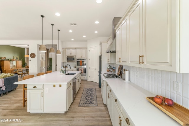 kitchen with pendant lighting, an island with sink, light hardwood / wood-style flooring, backsplash, and appliances with stainless steel finishes