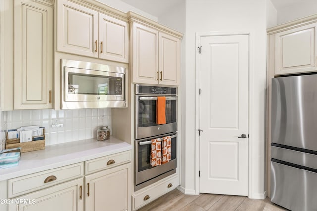 kitchen featuring appliances with stainless steel finishes, cream cabinetry, light hardwood / wood-style floors, and tasteful backsplash