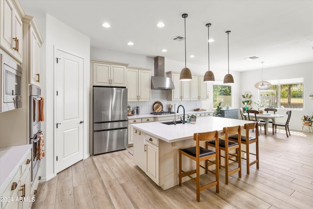 kitchen with decorative light fixtures, cream cabinets, stainless steel appliances, and wall chimney range hood