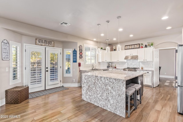 kitchen with light stone counters, pendant lighting, a kitchen island, white cabinetry, and sink