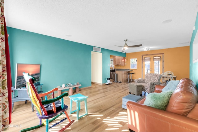 living room with french doors, ceiling fan, light hardwood / wood-style flooring, and a textured ceiling