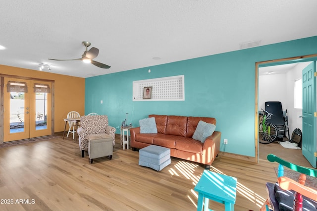 living room featuring ceiling fan, light hardwood / wood-style flooring, french doors, and a textured ceiling