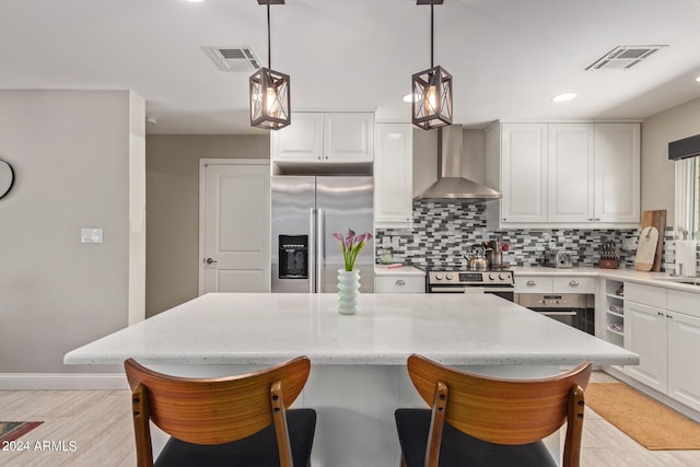 kitchen featuring appliances with stainless steel finishes, decorative light fixtures, wall chimney exhaust hood, white cabinets, and decorative backsplash