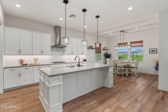 kitchen with visible vents, white cabinets, an island with sink, wall chimney exhaust hood, and a sink