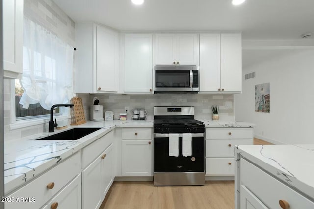 kitchen with appliances with stainless steel finishes, sink, white cabinets, decorative backsplash, and light stone counters