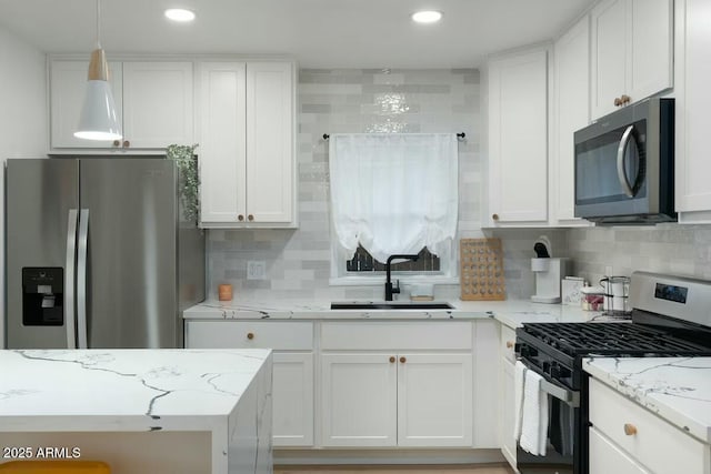 kitchen with sink, stainless steel appliances, light stone counters, white cabinets, and decorative light fixtures