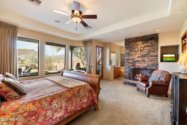 bedroom with a mountain view, ceiling fan, a stone fireplace, and light colored carpet