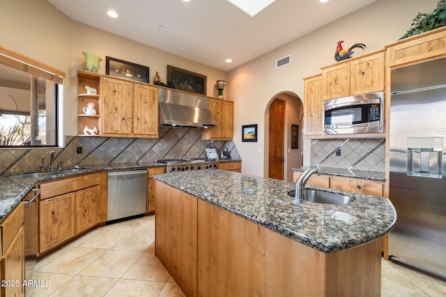 kitchen featuring built in appliances, a center island with sink, wall chimney exhaust hood, and sink