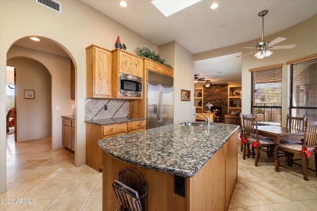 kitchen with built in appliances, a center island with sink, ceiling fan, and sink