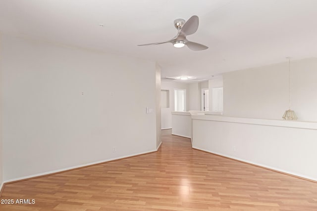 empty room with light wood finished floors, a ceiling fan, and baseboards