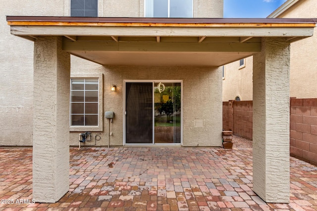 entrance to property featuring a patio area, fence, and stucco siding