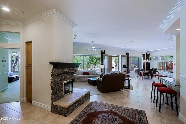 living room featuring crown molding, a fireplace, a ceiling fan, baseboards, and light tile patterned floors
