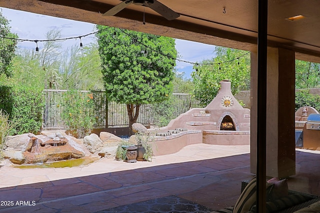 view of patio / terrace featuring ceiling fan, a lit fireplace, and a fenced backyard