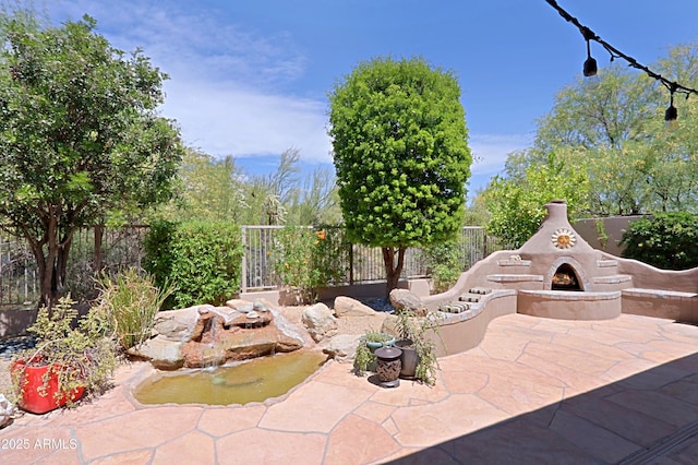 view of patio featuring fence and a warm lit fireplace