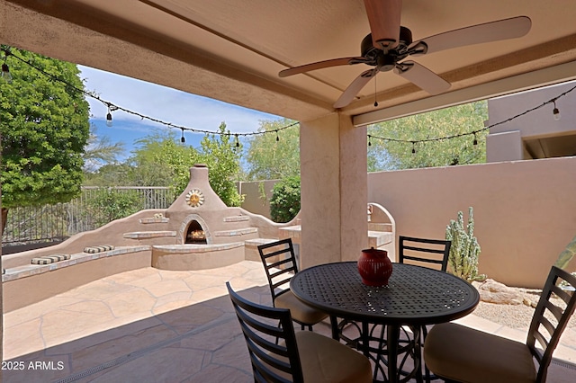 view of patio / terrace with a ceiling fan, a lit fireplace, a fenced backyard, and outdoor dining space
