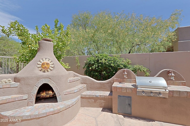 view of patio featuring a grill, a lit fireplace, exterior kitchen, and fence