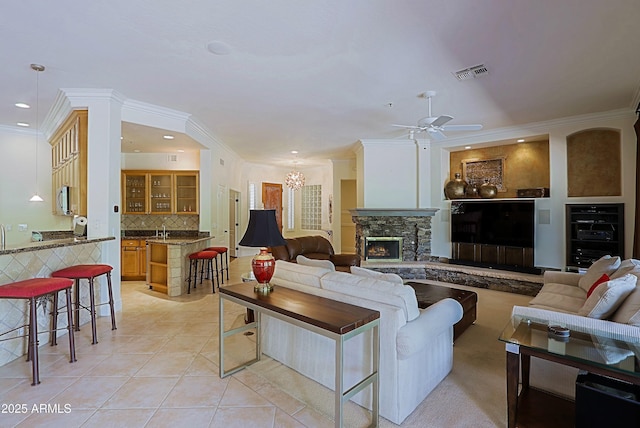 living area featuring visible vents, ornamental molding, light tile patterned floors, and ceiling fan with notable chandelier