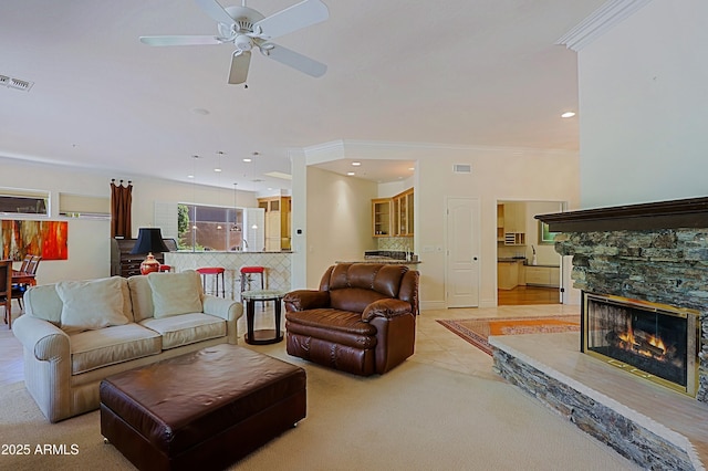 living area featuring visible vents, a ceiling fan, a fireplace, and ornamental molding
