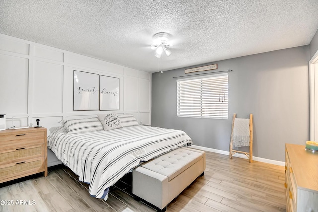bedroom featuring light wood-style flooring, a textured ceiling, baseboards, and ceiling fan