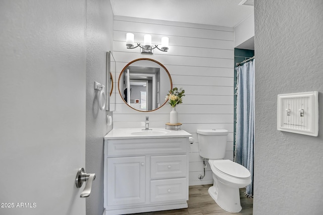 bathroom with toilet, wood finished floors, a textured wall, and vanity