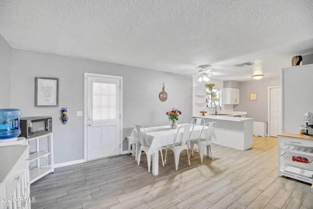 dining space with a textured ceiling, light wood finished floors, a ceiling fan, and visible vents
