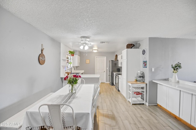 dining space with ceiling fan, light wood-style flooring, a textured ceiling, visible vents, and baseboards