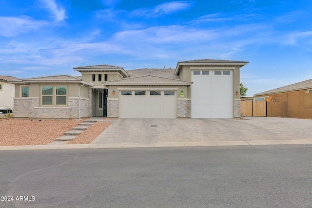 prairie-style house featuring a garage, driveway, stone siding, fence, and stucco siding