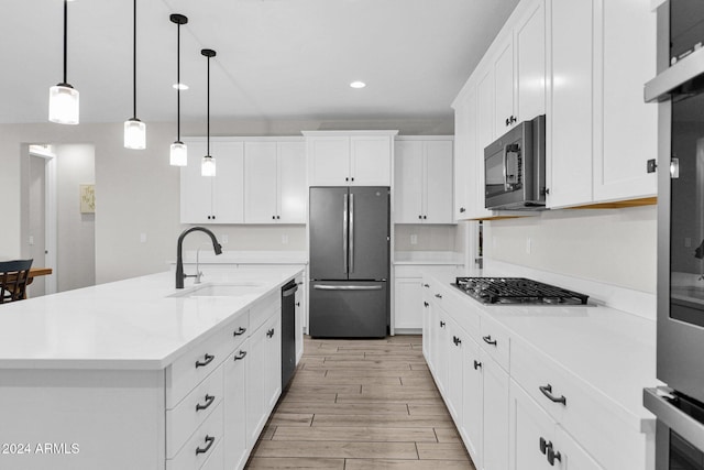 kitchen with appliances with stainless steel finishes, sink, a center island with sink, decorative light fixtures, and white cabinetry