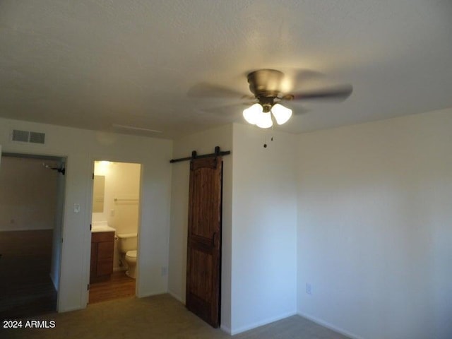 unfurnished bedroom with ensuite bath, a barn door, and ceiling fan