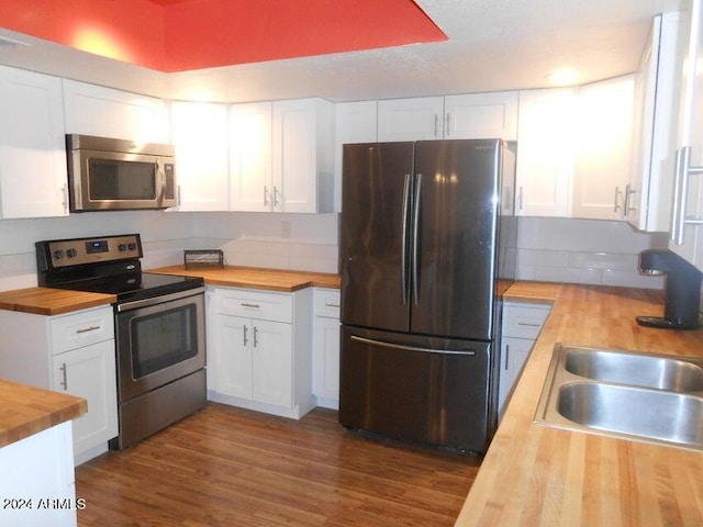 kitchen with appliances with stainless steel finishes, butcher block counters, sink, and white cabinets