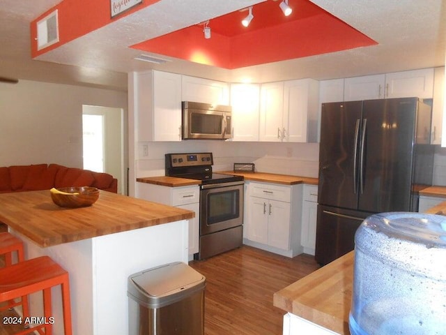 kitchen featuring white cabinetry, appliances with stainless steel finishes, a tray ceiling, and wooden counters