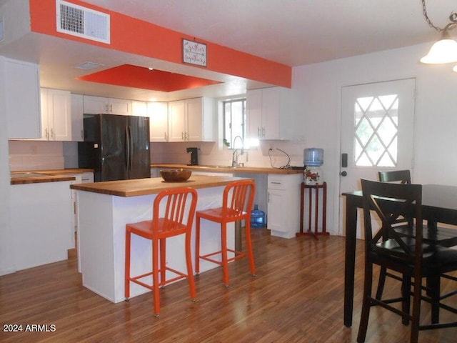 kitchen with a kitchen island, black fridge, white cabinets, and butcher block countertops