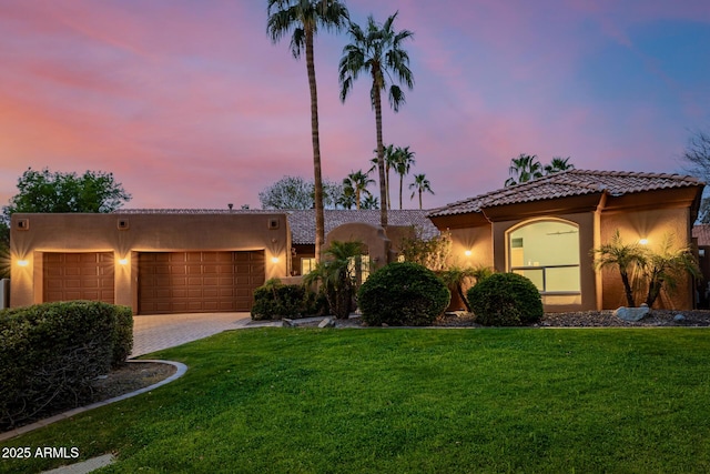 view of front of property with an attached garage, a lawn, decorative driveway, and stucco siding