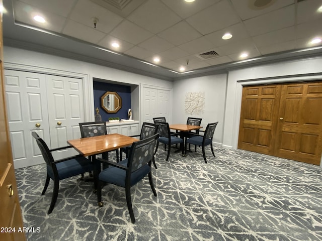 dining space with a paneled ceiling, ornamental molding, and dark colored carpet