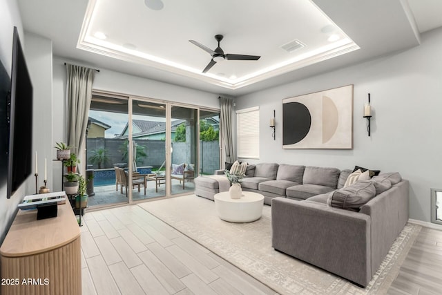 living area with visible vents, a ceiling fan, a tray ceiling, and wood finished floors