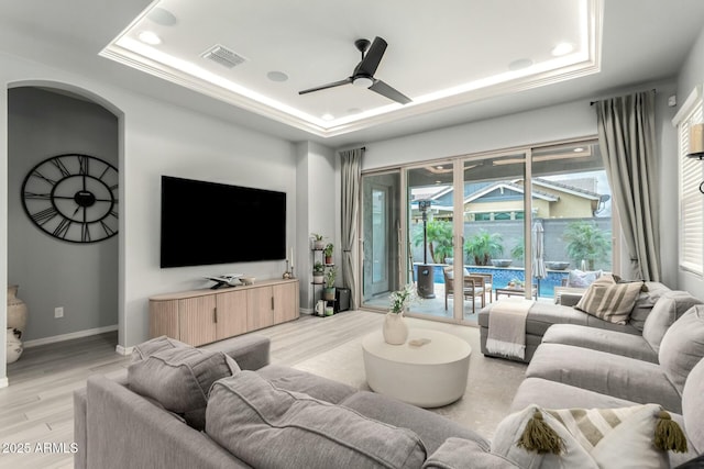 living area with a ceiling fan, visible vents, baseboards, a tray ceiling, and light wood-style flooring