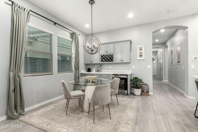 dining space featuring wine cooler, light wood-style floors, arched walkways, and baseboards