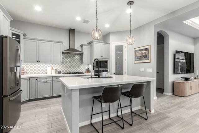 kitchen featuring wall chimney exhaust hood, arched walkways, appliances with stainless steel finishes, and gray cabinetry