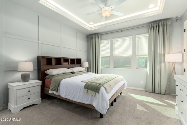 bedroom featuring a tray ceiling, ornamental molding, light carpet, a decorative wall, and a ceiling fan