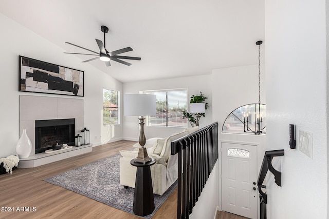 living room with ceiling fan with notable chandelier, a tiled fireplace, wood-type flooring, and vaulted ceiling