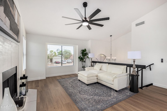 living room with ceiling fan with notable chandelier, hardwood / wood-style flooring, vaulted ceiling, and a tile fireplace